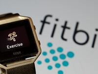 A Fitbit device in front of the Fitbit logo.
