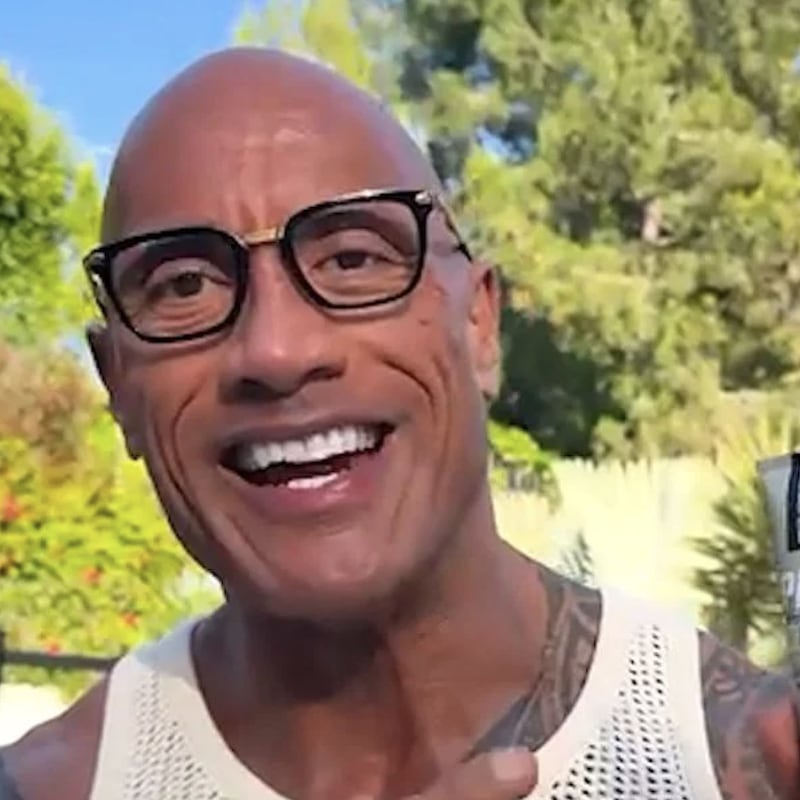 Dwayne "The Rock" Johnson holding PAPATUI Exfoliating Facial Scrub tube outdoors, smiling.