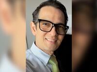 Pedro Argote smiles while wearing glasses and a shirt and tie.