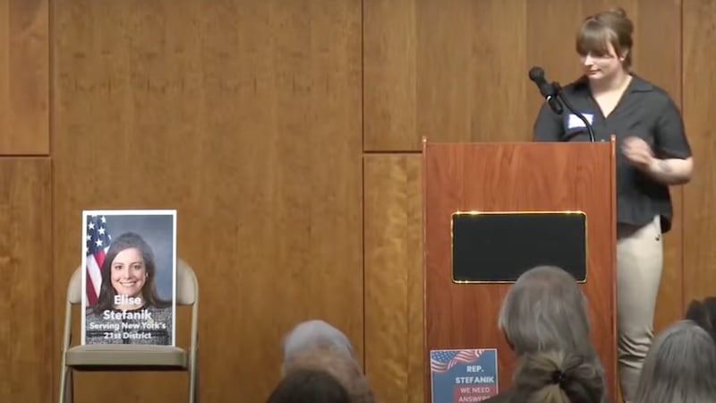 A picture of Rep. Elise Stefanik sitting on an empty chair next to a podium.