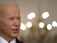 President Joe Biden talks to reporters with chandelier in the background.