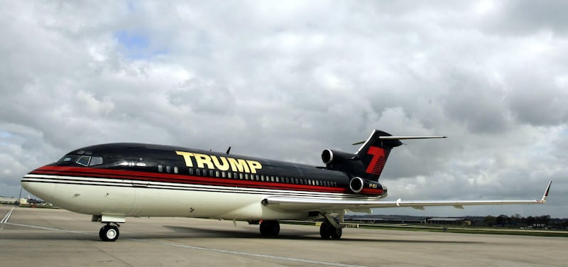 A Boeing 727 on tacam in the livery of Trump, with a white belly, black upper body and gold trimming.