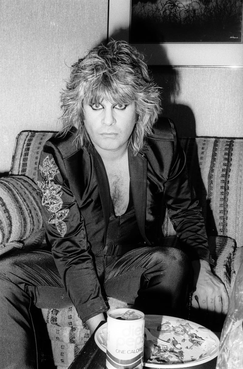 Ozzy Osbourne circa 1970 wearing an all-black outfit, black eyeliner, and a shaggy haircut.