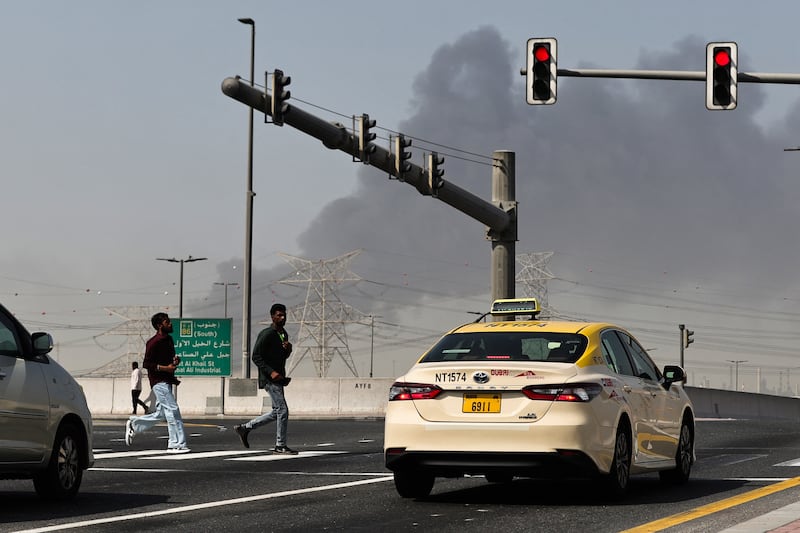 People cross a street as smoke rises from the site of a reported Iranian strike in Dubai on March 1, 2026