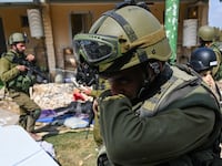An IDF soldier covering his nose in front of a house.